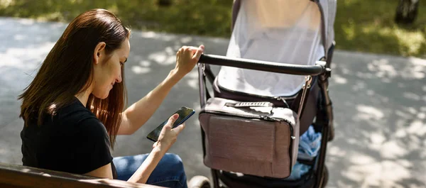 young mother, woman with stroller with smartphone in hands sitting on Park bench, maternity leave concept, for banner