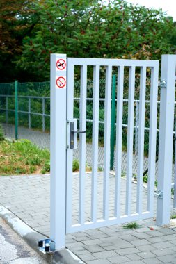 Kapı kolu, kilidi ve direkte iki uyarı levhası olan modern metal kapı: köpek ve sigara yasak. Kentsel altyapı ayrıntıları güvenliği, düzenlemeleri ve kamu kurallarını sembolize ediyor.