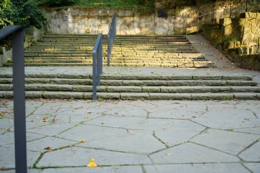 Parktaki eski taş merdivenler, yosun ve yapraklarla kaplı, yukarı doğru metal tırabzanlarla çıkıyor..