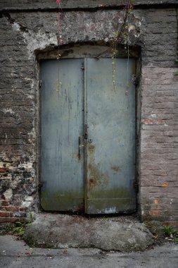 Yıpranmış tuğla duvarda eski paslı metal kapı, soyulmuş boya, dokulu kentsel arka plan ve grunge mimari detayları..