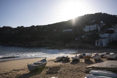 Sabah güneşi çam ağaçlarıyla kaplı bir tepenin arkasında yükselirken sakin bir Akdeniz sahili ve sakin bir sahil köyünü aydınlatıyor.