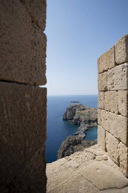 Turkuaz su sarp kayalıkları ve sahil kenarındaki park alanının doğa ile çevrili olduğu ve berrak bir yaz gününde engin, huzurlu bir okyanus tarafından çerçevelendiği Akdeniz burnu manzarası.