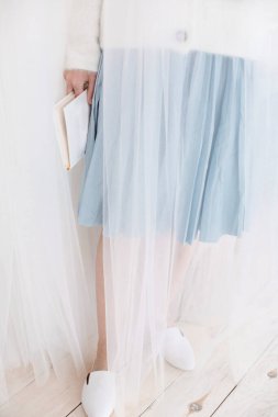 Etekli ve ayakkabılı bir kız dergi okuyor, kadın ince bacakları süet katırlar ve düz mokasenlerle, bir odada bir koltukta ya da koltukta oturuyor ve elinde bir bardak ve bir dergi tutuyor.