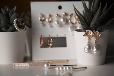 İnci, küpe ve saç tokaları olan modern stil pahalı ve lüks altın mücevherlerin bir koleksiyonu, kapalı alan çiçeklerinin arka planında, bir kadının masasında yatıyor.
