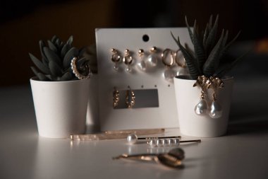 İnci, küpe ve saç tokaları olan modern stil pahalı ve lüks altın mücevherlerin bir koleksiyonu, kapalı alan çiçeklerinin arka planında, bir kadının masasında yatıyor.
