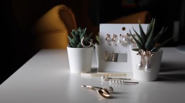 İnci, küpe ve saç tokaları olan modern stil pahalı ve lüks altın mücevherlerin bir koleksiyonu, kapalı alan çiçeklerinin arka planında, bir kadının masasında yatıyor.