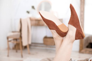 Topuksuz, katırsız ve mokasensiz şık kadın ayakkabıları, kadın bacakları üzerinde, elbise ve ayakkabı giymiş bir kız, yatak odasında dinleniyor, dergi okuyor, reklam için trend ayakkabıları, bir sepetin içinde