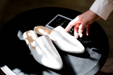 Bloglar için siyah arka planda beyaz ayakkabılar, bir parmak ayakkabı, bir el gölgesi, fiyat etiketi veya yazıtlar için boş bir yeri olan bir tabak, günlük deri ayakkabılar