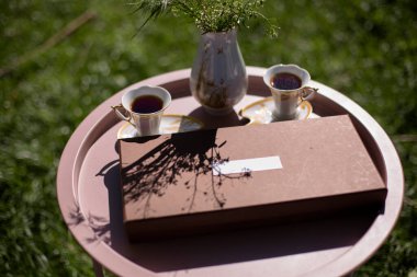 İnce yaz kadınlarının bej benekli eldivenleri sokaktaki çay masasının üzerinde hediye kutusunun yanında ve bir fincan kahve ya da çay klasik tarzda sokakta çimenlerin ve bahçenin arka planında