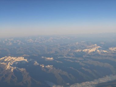 Nefes kesen bir manzarada güneş ışığıyla yıkanmış görkemli dağ sıraları, yukarıda açık gökyüzü ve sabahın erken saatlerinde arazide oynayan nazik gölgeler görülüyor..