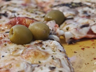 Pizza erimiş peynirle yeni pişirildi ve yeşil zeytin ve otlarla kaplandı, kırsal ahşap bir masada dinleniyor. İştah açıcı renkler lezzetli bir cazibe yaratır..