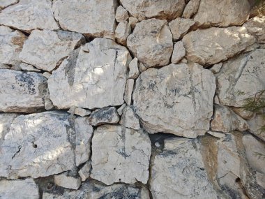 Değişik boyutlarda ve şekillerde kayaların sergilendiği engebeli taş bir duvar. Güneş ışığı, duvarın doğal güzelliğini açık bir ortamda ortaya çıkararak dokuyu vurgular..