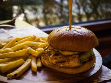 Taze marullu ızgara tavuk burger ve yanında da bol miktarda kızarmış patates. Bu lezzetli yemek, rahat bir ortamda öğle yemeği için mükemmel..