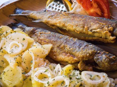 Two perfectly cooked trout are served with seasoned potato slices and garnished with onions and herbs. This dish showcases local cuisine in a charming restaurant.