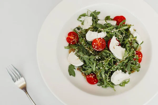 Ensalada fresca con rúcula, tomates cherry, queso mozzarella y nueces sobre blanco. Vista superior —  Fotos de Stock