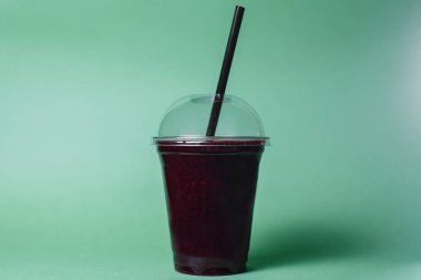 disposable cup of berry smoothie with straw on studio background