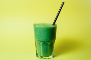 glass of smoothie with straw on green studio background