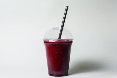 disposable cup of beetroot smoothie with straw on studio background
