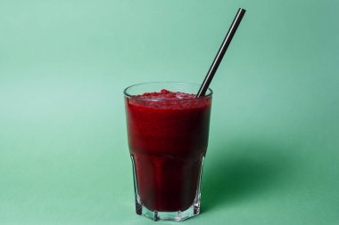 glass of smoothie with straw on green studio background