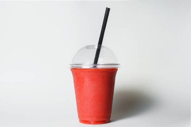disposable cup of strawberry smoothie with straw on studio background