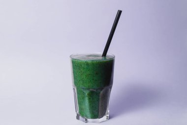 glass cup of green smoothie with straw on studio background