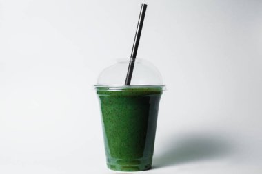 disposable cup of green smoothie with straw on studio background