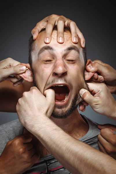 many hands making funny face on man, stretching face skin