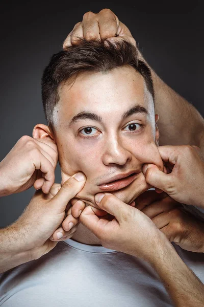 many hands making funny face on man, stretching face skin