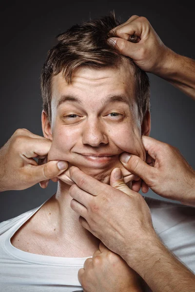 many hands making funny face on man, stretching face skin