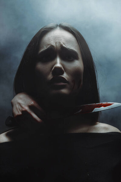 испуганная женщина с рукой, держащей окровавленный нож за шею
