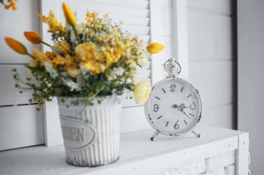 Beyaz bir masada sarı çiçekli bir çalar saat. Kaliteli fotoğraf
