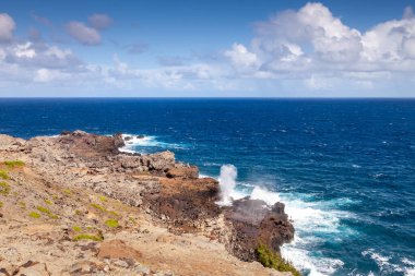 The breathtaking northern coastline of Maui features rugged rocks and foaming waves crashing against the shore and Nakalele blowhole shooting water.