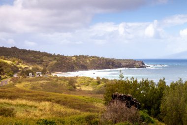 Vibrant green hills roll down to meet the clear blue ocean along the northern coast of Maui. Coastal roads wind through this serene paradise, inviting exploration and adventure in nature.