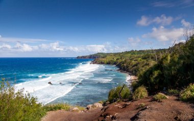 Explore the stunning northern coast of Maui around Poelua Bay where turquoise waves crash against rocky shores. Lush greenery complements the serene landscape under a clear sky, perfect for nature enthusiasts.