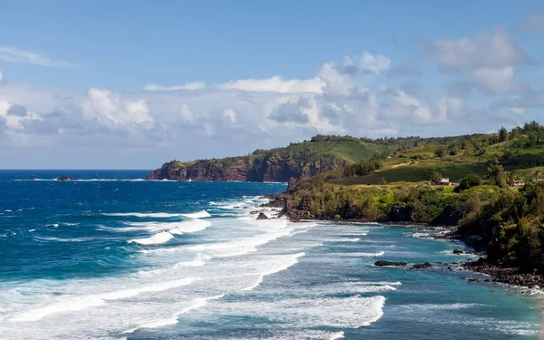 Explore the stunning north coast of Poelua Bay in Maui where waves crash against rocky shores, framed by vibrant green hills and a clear blue sky, perfect for nature lovers and adventure seekers alike.