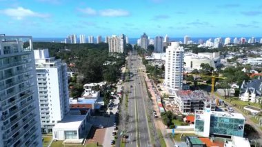 Punta del Este 'nin ana arterlerinden Roosevelt Bulvarı boyunca Punta Alışveriş' e doğru giden dinamik insansız hava aracı uçuşu. Ufukta ünlü ikonik Torre Lafayette duruyor.