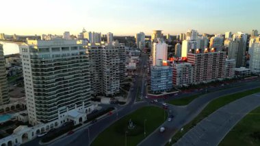 Los Dedos anıtı yakınlarındaki Playa Brava boyunca insansız hava aracı uçuşu Punta del Este 'nin ikonik siluetini vurguluyor. Ön planda, neoklasik tabanlı lüks Yapılandırma kuleleri yükselir.