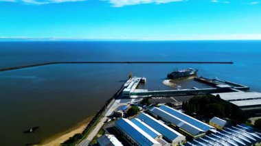 İHA görüntüleri, Colonia del Sacramento, Uruguay feribot terminalini ve liman tesislerini yakalar. Sahne iskeleye yanaşmış feribotları, endüstriyel depoları ve koruyucu dalgakıranları gösteriyor.