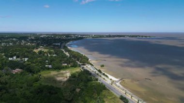 Colonia del Sacramento Uruguay kıyı şeridinin geniş hava görüntüsü. Kıyı şeridi Rio de la Plata 'nın kumlu sahilleri ve sığ sularıyla uzanır. Kıyı yolu ağaçlar ve palmiyelerle doluydu.