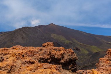 Kayalık ön planda dramatik volkanik manzara ve mavi gökyüzüne karşı hareketsiz bir volkanın karanlık yamaçları. Engebeli arazi doğal güzelliği ve jeolojik mucizeyi yakalar..