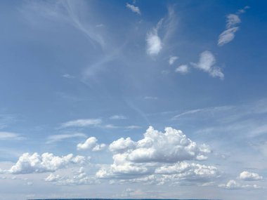 Parlak mavi gökyüzü ve dağınık beyaz bulutlar. Hava, özgürlük ve doğal güzelliği temsil eden huzurlu bir atmosfer..