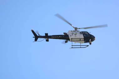 Los Angeles, USA - August 16, 2025: Black and white helicopter flying against a clear blue sky, captured in motion with spinning rotor blades.
