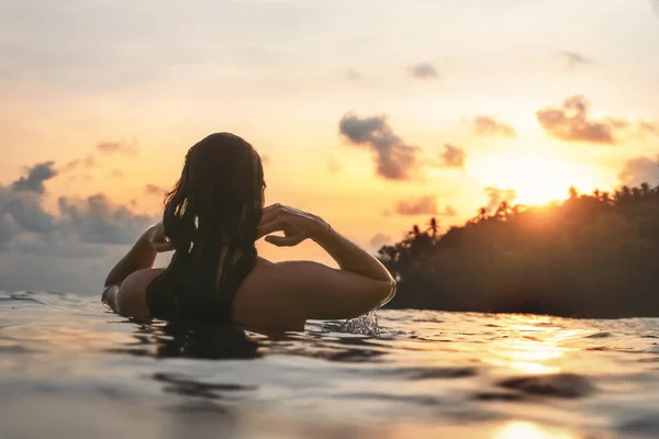 young woman from behind in indian ocean bathing and holding her hair during orange sunset with romantic mood