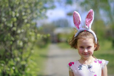 Paskalya gününde tavşan kulağı takan şirin bir çocuk. Baharda çiçek açan bahçelerin arka planında güzel kıvırcık saçlı kız.