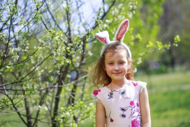 Paskalya gününde tavşan kulağı takan şirin bir çocuk. Baharda çiçek açan bahçelerin arka planında güzel kıvırcık saçlı kız.