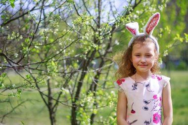 Paskalya gününde tavşan kulağı takan şirin bir çocuk. Baharda çiçek açan bahçelerin arka planında güzel kıvırcık saçlı kız.