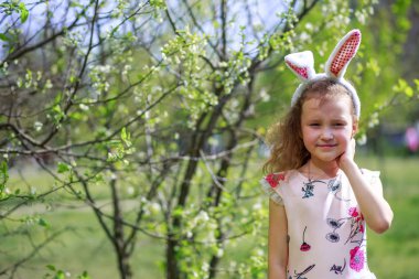 Paskalya gününde tavşan kulağı takan şirin bir çocuk. Baharda çiçek açan bahçelerin arka planında güzel kıvırcık saçlı kız.