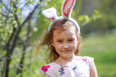 Paskalya gününde tavşan kulağı takan şirin bir çocuk. Baharda çiçek açan bahçelerin arka planında güzel kıvırcık saçlı kız.