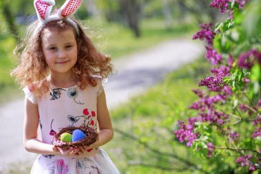Paskalya yumurtalarının olduğu sepeti tutan bir kız. Çocuk Paskalya Tavşanı 'nın yumurtalarının ilkbaharında sokakta toplandı. Paskalya günü tavşan kulağı takan şirin bir çocuk..
