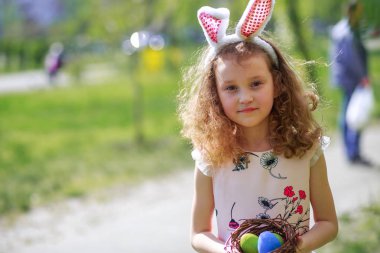 Paskalya yumurtalarının olduğu sepeti tutan bir kız. Çocuk Paskalya Tavşanı 'nın yumurtalarının ilkbaharında sokakta toplandı. Paskalya günü tavşan kulağı takan şirin bir çocuk..